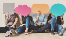 a group of four seated creatives hold up colourful paper cut outs of speech bubbles, covering their faces - header image from the graphic design blog by nstudio