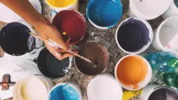 A man dipping a paintbrush into a paint container, taking brown paint - header image from the graphic design blog by nstudio