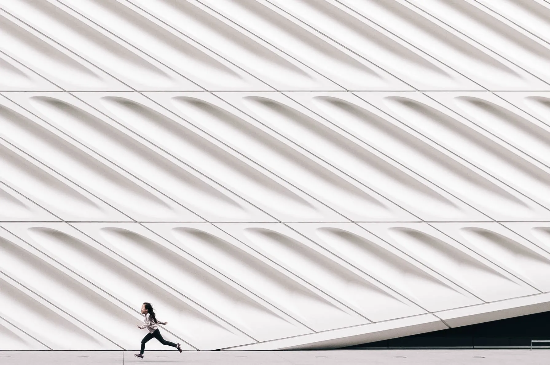 A girl, small in the frame, runs in front of a modern building