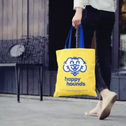 a woman walks down the street holding a yellow happy hounds branded tote bag