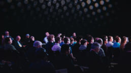 Crowd of people sitting inside an auditorium, attending a presentation