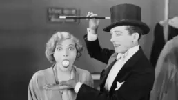 a vintage black and white photograph of a magician and his female assistant, who is surprised to have an have an egg in her mouth