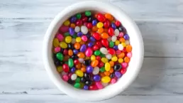 a bowl of colourful jelly beans sits on a timber floor