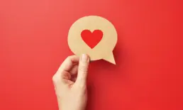 a heart printed on a piece of paper cut into a speech bubble, held by a hand