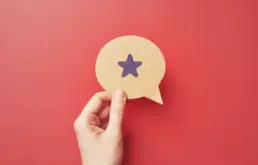 a hand holds a cut out of a speech bubble with a star icon drawn on it