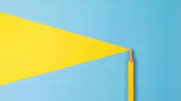 A yellow colouring pencil laid on blue and yellow card