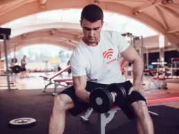 a male lifts weights while wearing a t-shirt, which has the tephra logo design on the left chest