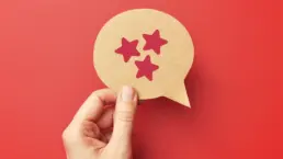 a hand holds a cut out of a speech bubble with three stars drawn on it