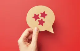a hand holds a cut out of a speech bubble with three stars drawn on it