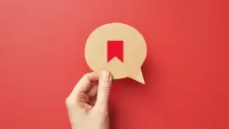 a hand holds a cut out of a speech bubble with a bookmark icon drawn on it