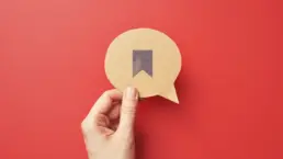 a hand holds a cut out of a speech bubble with a bookmark icon drawn on it
